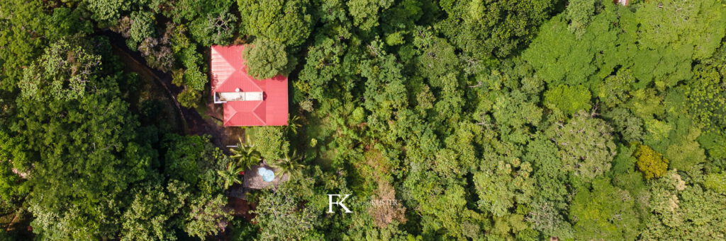 Aerial view of a home with a red roof surrounded by dense forest canopy in Costa Rica