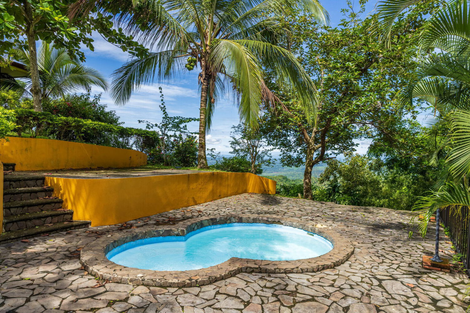 Stone-paved pool terrace framed by palms above the coastal jungle