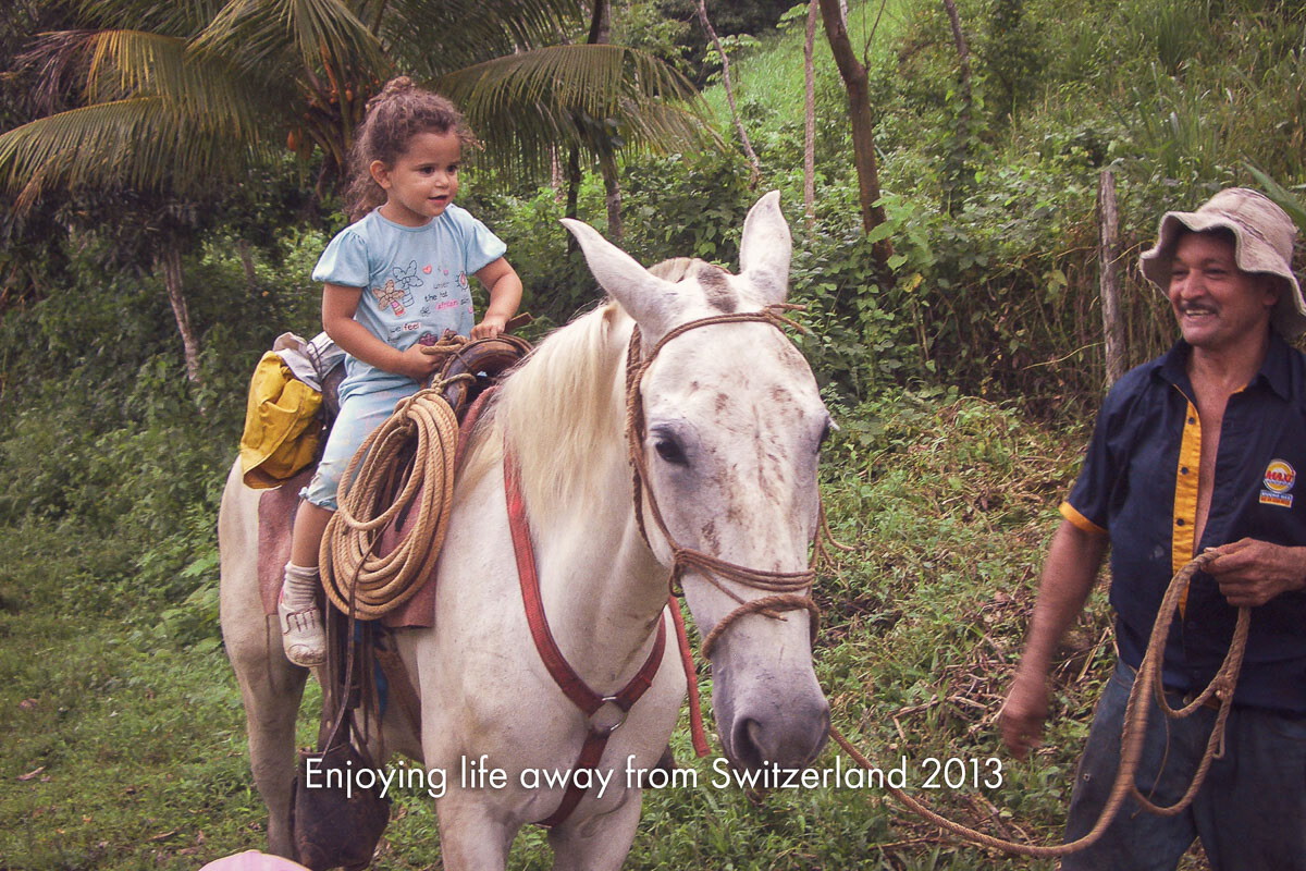 A small child riding a white horse led by a farmer along a jungle track