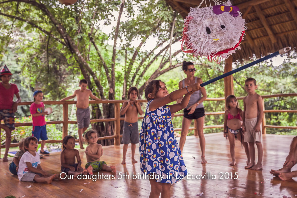 Children gathered around a piñata at a birthday party under a timber roof