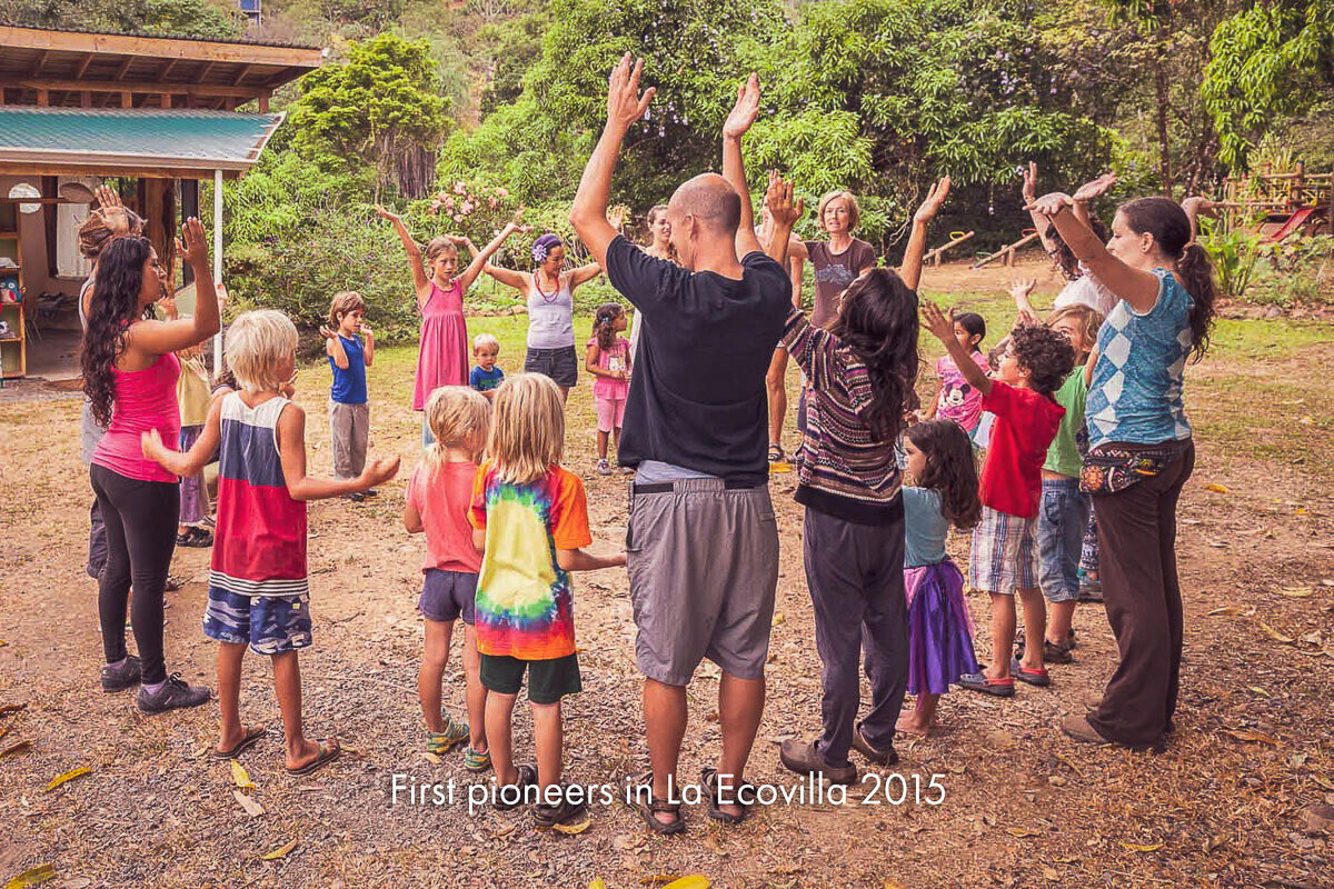 Adults and children standing in a circle on open ground with their arms raised