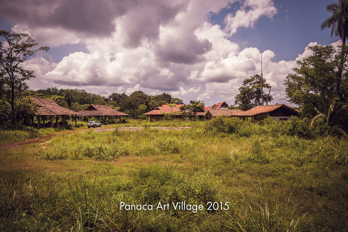 Low red-roofed buildings across open grassland under a cloudy sky