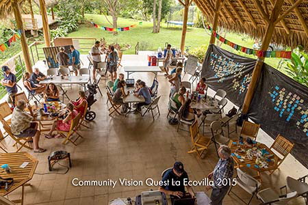 Community members meeting at tables under an open thatched pavilion