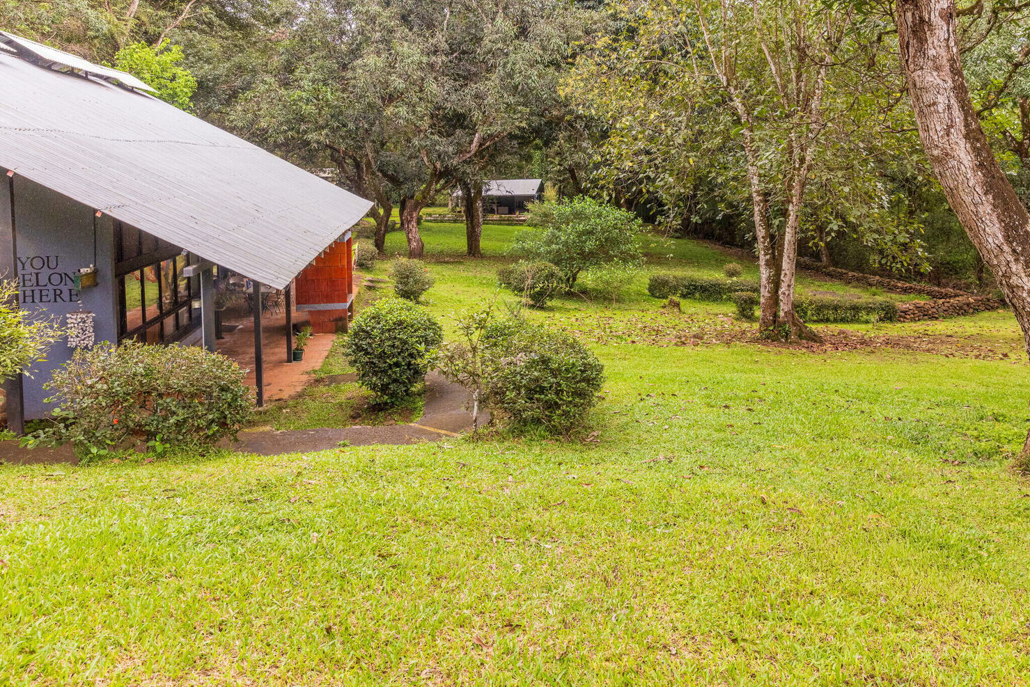Painted building exterior with a covered walkway beside open lawn and trees